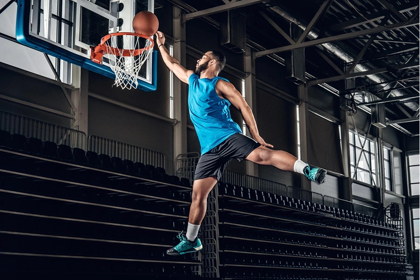 Atleta de basquetebol a realizar um poderoso afundanço numa arena desportiva fechada.